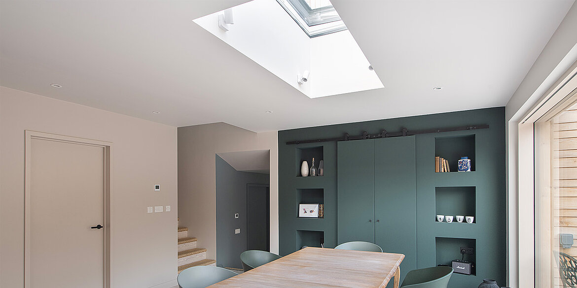 Green kitchen units with dining table and glass skylight above
