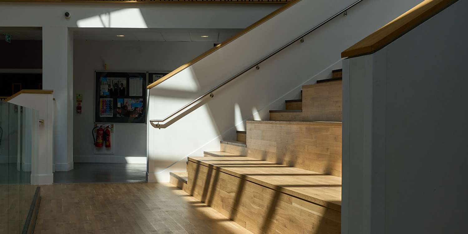Natural daylight from LAMILUX rooflights illuminating timber seating and stairs in a modern school atrium